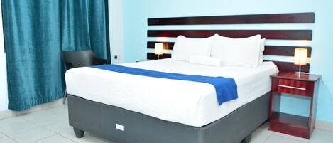 A hotel room with a bed, a nightstand, a chair, and a window with curtains.