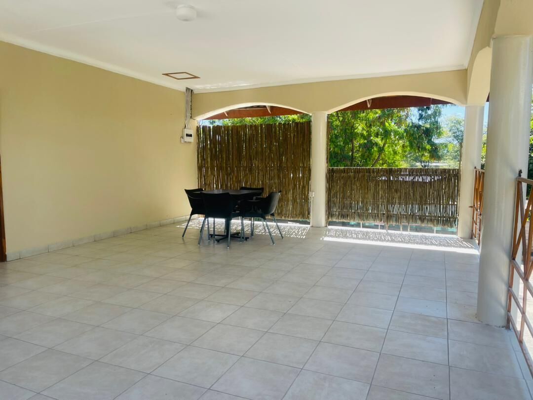 Un patio abierto con suelo de baldosas, una mesa y sillas negras, y una valla de bambú.