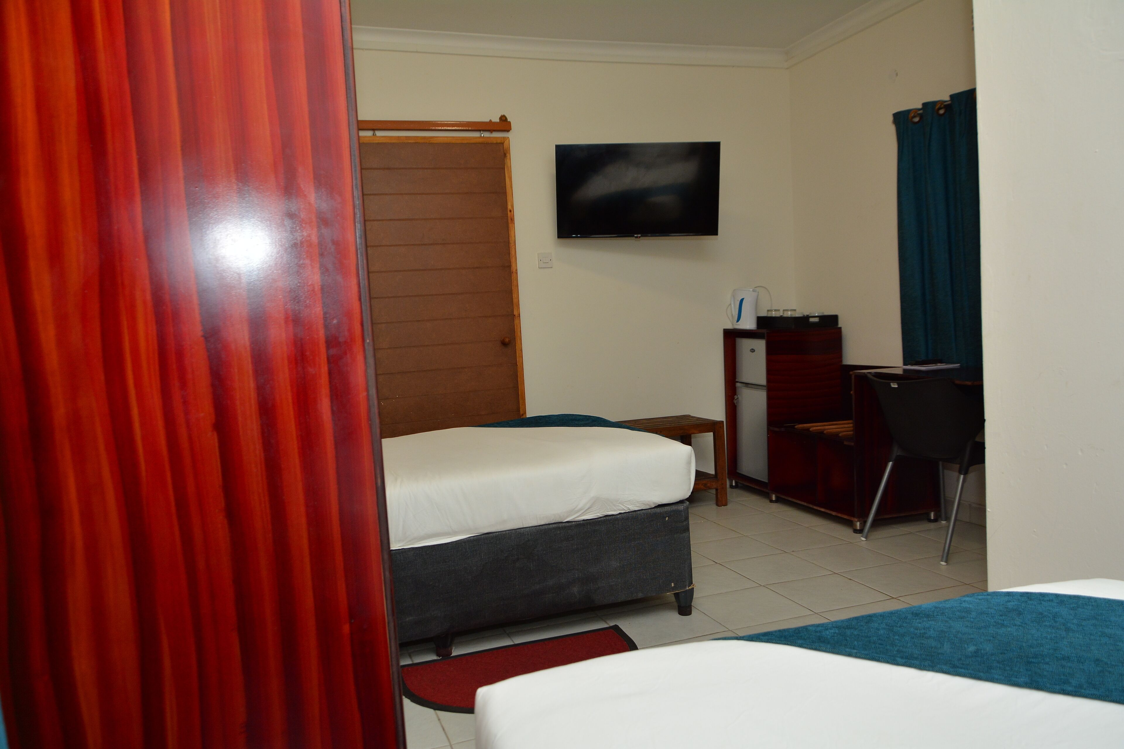 A hotel room with two beds, a desk, a chair, a TV, and a wardrobe.