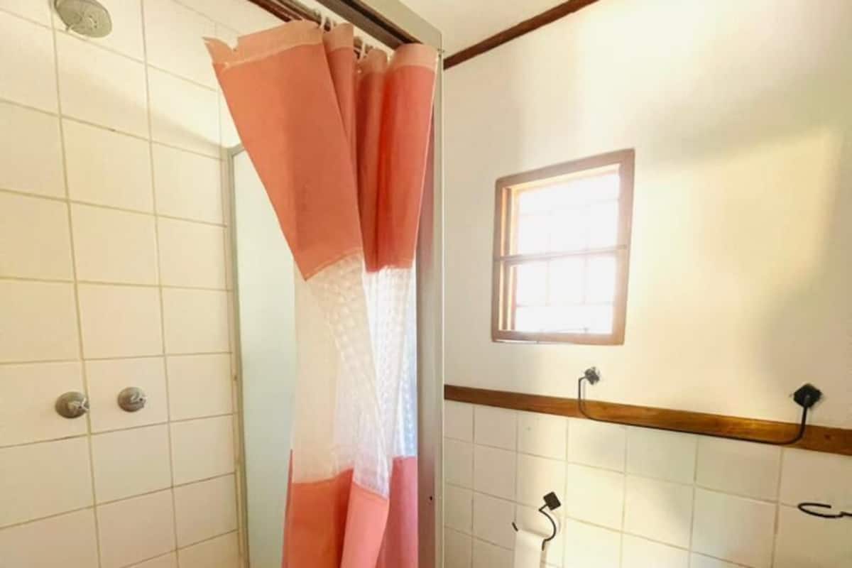 A bathroom with a shower curtain, a toilet, a sink, and a window.