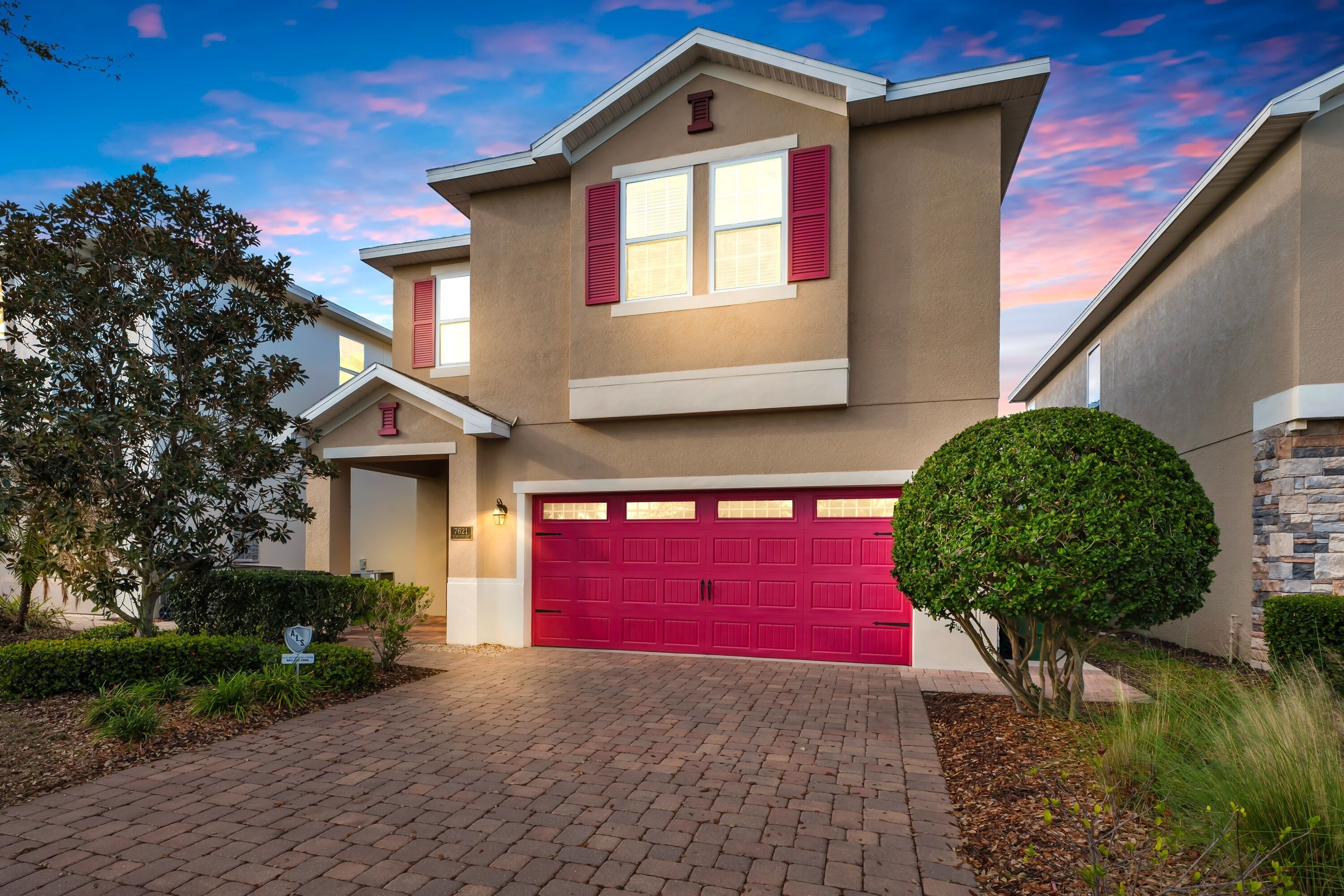 A modern two-story house with a red garage door, a small front porch, and a well-maintained garden.