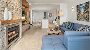 A modern living room with a stone fireplace, a blue sofa, and a dining area with a white table and chairs. - Byron Bay Accom - Forty Five on Lawson Apt 7 (Byron Bay)