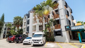 A multi-story building with a modern architectural design, featuring balconies and large windows. There are several vehicles parked in front, including a white van and a red SUV. - Cozy Studio in Gazcue, Steps to Zona Colonial (Santo Domingo)