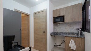 A compact kitchen with a microwave, wooden cabinets, and a small countertop. - Cozy Studio in Gazcue, Steps to Zona Colonial (Santo Domingo)