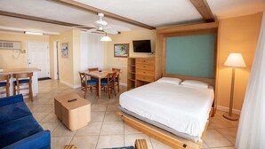 A hotel room with a bed, a desk with chairs, a television, and a ceiling fan. - Oceanfront Studio w/ Balcony in Daytona Beach (Daytona Beach Shores)