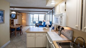 A compact kitchen with a stove, microwave, and sink. There is a dining area with a table and chairs, and a sofa with a view of the ocean. - Oceanfront Studio w/ Balcony in Daytona Beach (Daytona Beach Shores)