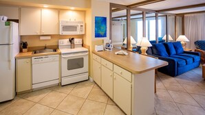 A compact kitchen with a microwave, stove, and dishwasher, a small dining area with a table and chairs, and a blue sofa in the living area. - 1BR Oceanfront Condo w/ Full Kitchen & Balcony (Daytona Beach Shores)