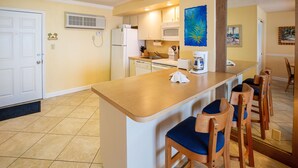 A compact kitchen with a central island, white appliances, and wooden chairs. - 1BR Oceanfront Condo w/ Full Kitchen & Balcony (Daytona Beach Shores)