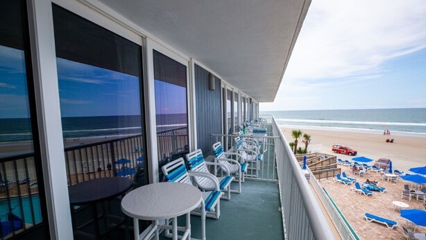 Un balcón con vista a la playa, con sillones y mesas.