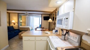 Habitación de hotel compacta con kitchenette, cama, sofá y televisor.