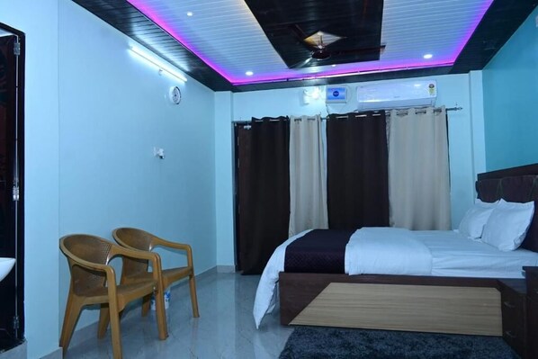 Une chambre à coucher comprenant un lit, deux chaises, une table de chevet, un ventilateur de plafond et un appareil de climatisation.