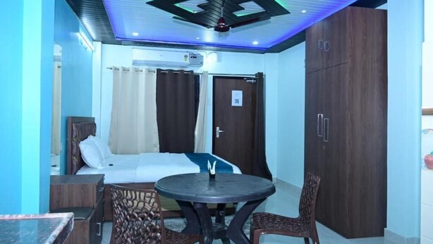 A hotel room with a bed, a round table with two chairs, a wardrobe, and a ceiling fan. - White stay house  (Azamgarh)