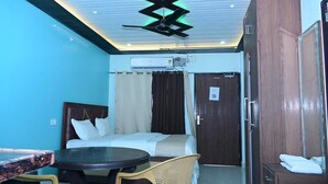 A hotel room with a bed, a small table, a chair, a wardrobe, and a ceiling fan. - White stay house  (Azamgarh)