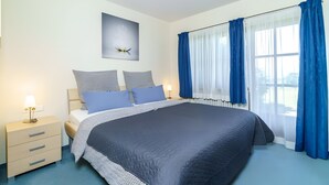 Een slaapkamer met een groot bed, een nachtkastje met een lamp en een raam met blauwe gordijnen.