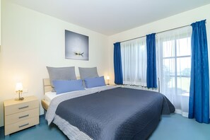 Ein Schlafzimmer mit einem großen Bett, einem Nachttisch mit Lampe und einem Fenster mit blauen Vorhängen.