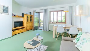 Een moderne woonkamer met een bank, een salontafel, een televisie en een eethoek met stoelen en een tafel.