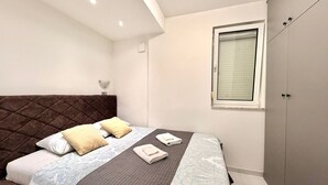 A bedroom with a large bed, a headboard, a window, and a wardrobe. - Adriatic Central 2BDR Apartment (Budva)