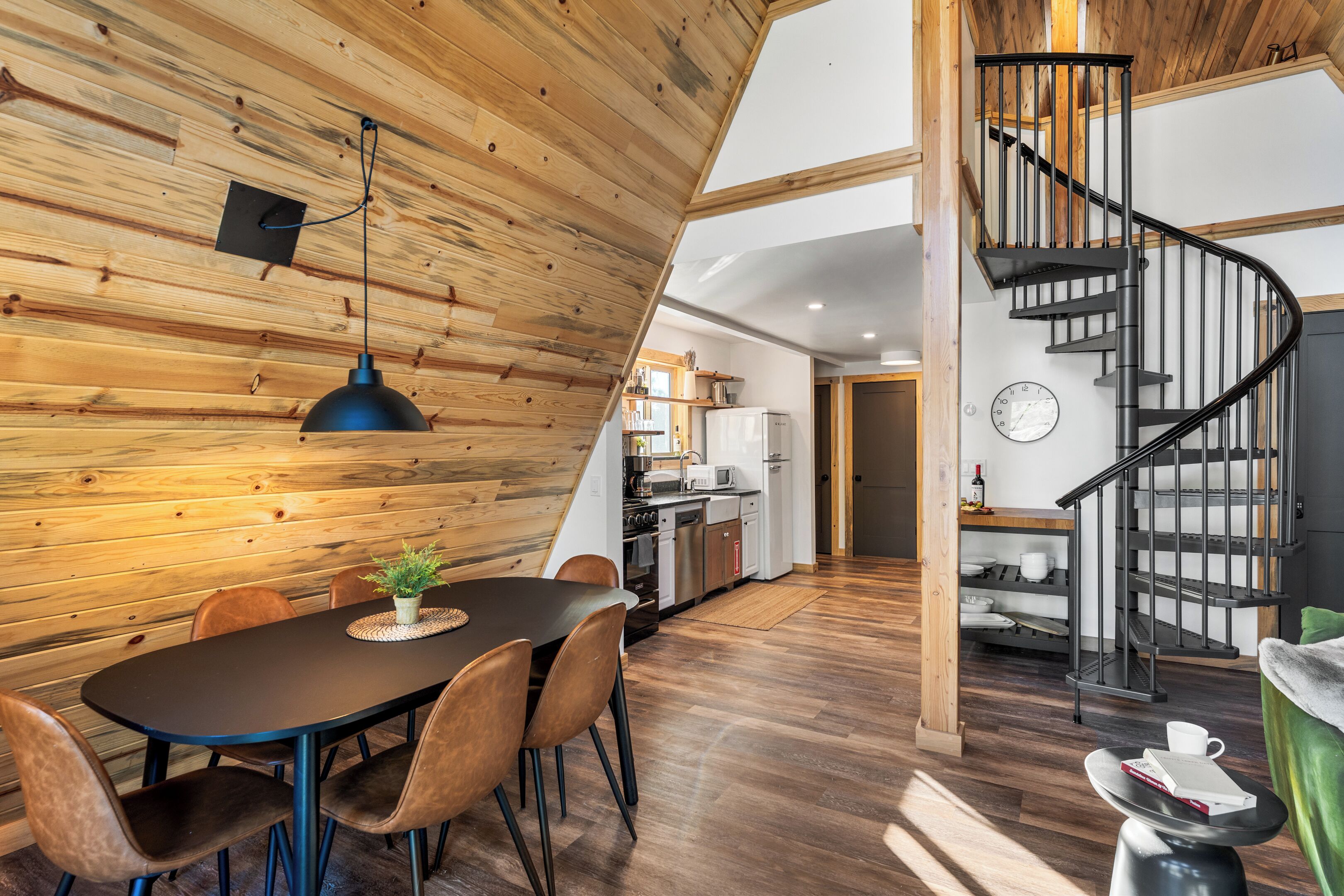 Una cocina moderna con techo de madera, un comedor con mesa y sillas, y una escalera de caracol.