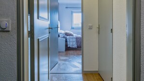 Un couloir au plancher de bois menant à une chambre à coucher équipée d’un lit et d’une fenêtre.