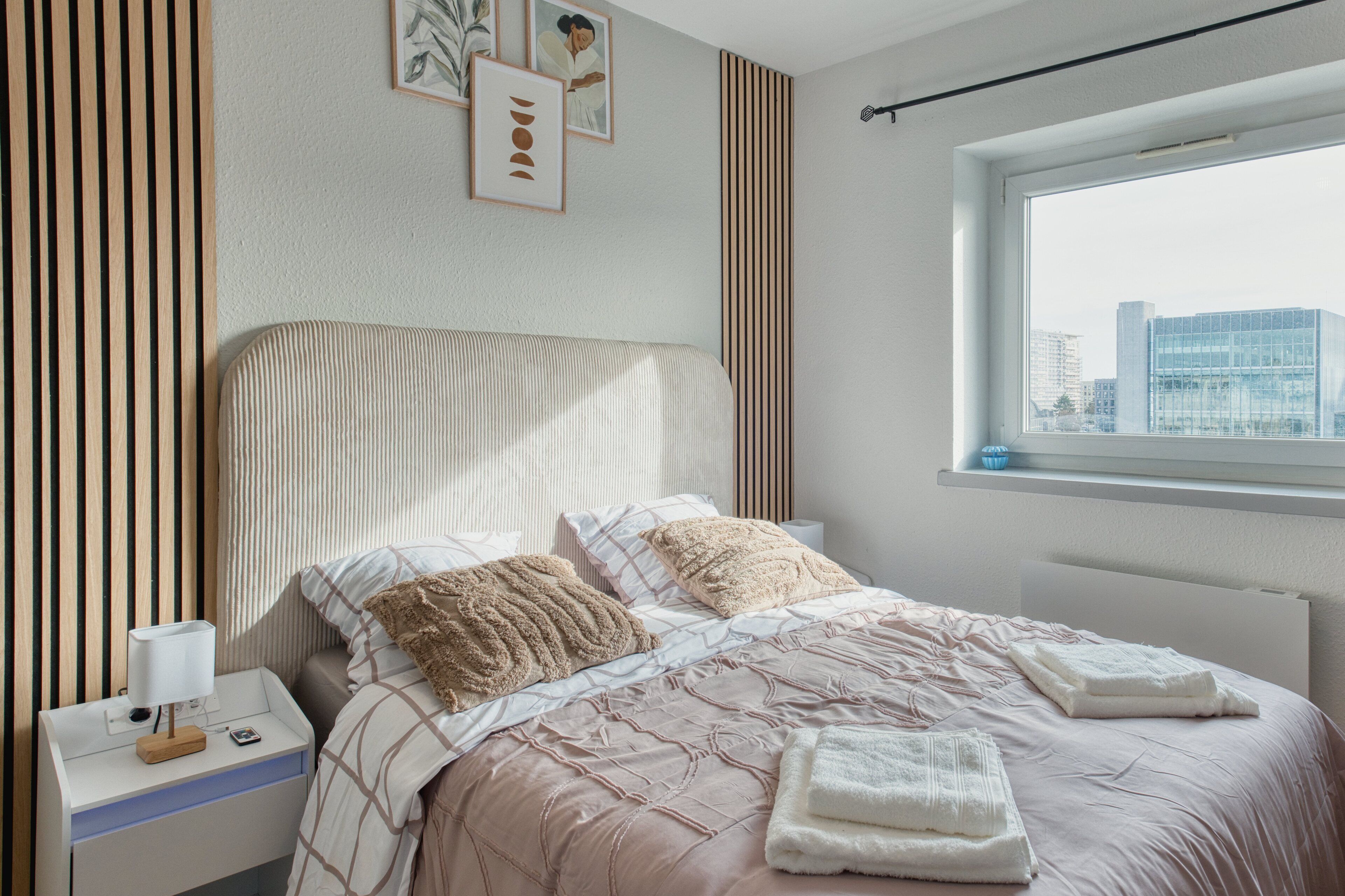 Una camera da letto ordinata con un letto, un comodino e una finestra vista città.