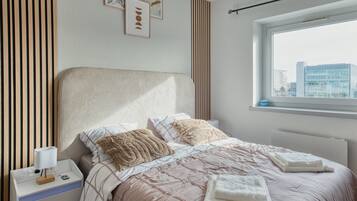 Una camera da letto ordinata con un letto, un comodino e una finestra vista città.