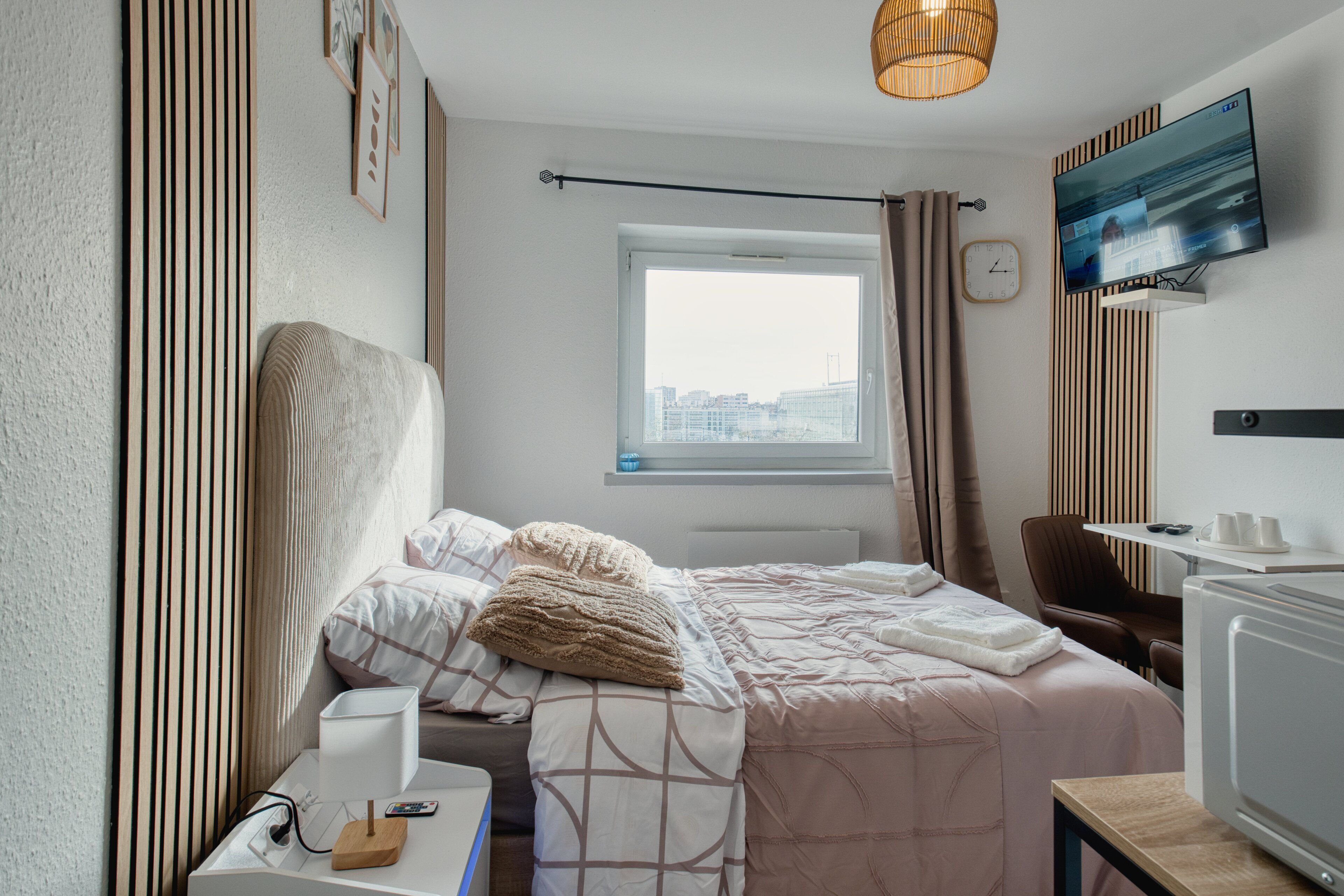 Una habitación de hotel moderna con cama, mesita de noche, televisor y ventana con cortinas.