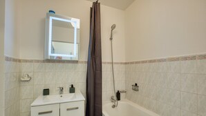 Une salle de bain avec un lavabo blanc, un miroir et une baignoire.