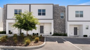 A modern multi-story building with a parking lot and landscaped areas. - Modern 4BR Home + Pool + Parking Disney 15min (Davenport)