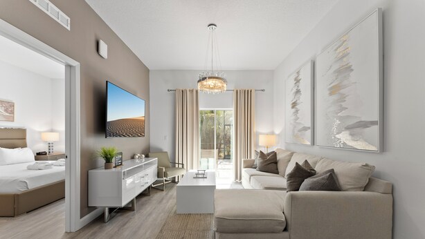 A modern hotel room with a bed, a sofa, a TV, a chandelier, and artwork on the walls. - Modern 4BR Home + Pool + Parking Disney 15min (Davenport)
