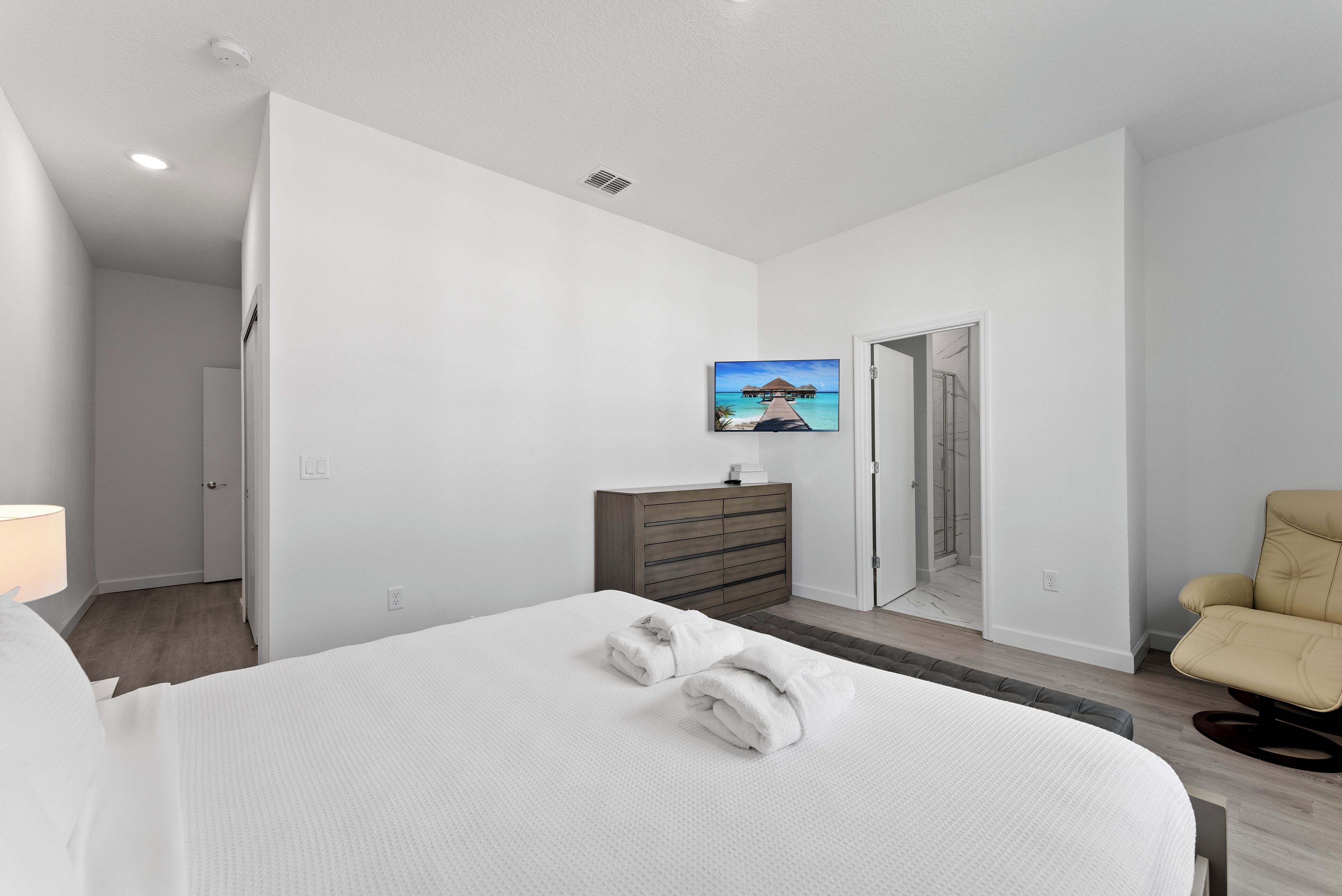 A modern hotel room with a large bed, a wooden dresser, a chair, and a painting on the wall.