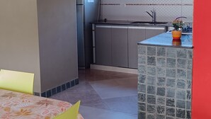 A kitchen with a refrigerator, a sink, and a window. There is a dining table with chairs and a tiled backsplash. - Sea house (Miramar)