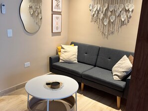 A modern living room with a grey sofa, a round white coffee table, and wall art including a macrame piece and framed abstract designs. - Centro Playa Del Carmen Duna  206 (Playa del Carmen)