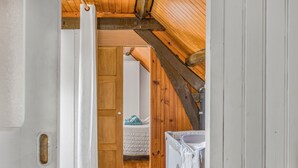 Een houten interieur met een witte deur, een bed met een blauwe deken en een witte dressoir.