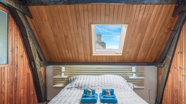 Een kleine, gezellige kamer met een schuine kap, dakraam, bed met sprei en twee opgevouwen handdoeken op het bed.