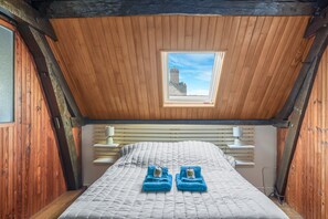 A small, cozy room with a sloped ceiling, a skylight, a bed with a quilt, and two folded towels on the bed.