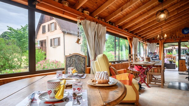 Un interior de madera con una mesa de comedor para dos, una silla y vista a una casa afuera.