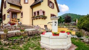 Un edificio amarillo con una escalera de piedra, una fuente y macetas con flores.