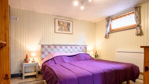 A bedroom with a bed, bedside lamps, a window with curtains, a wall-mounted painting, and a radiator.