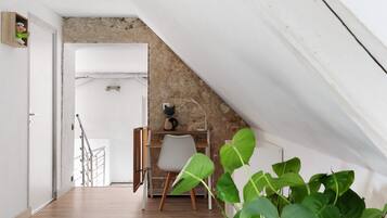 A room with a sloped ceiling, a white door, a desk with a chair, and a plant.