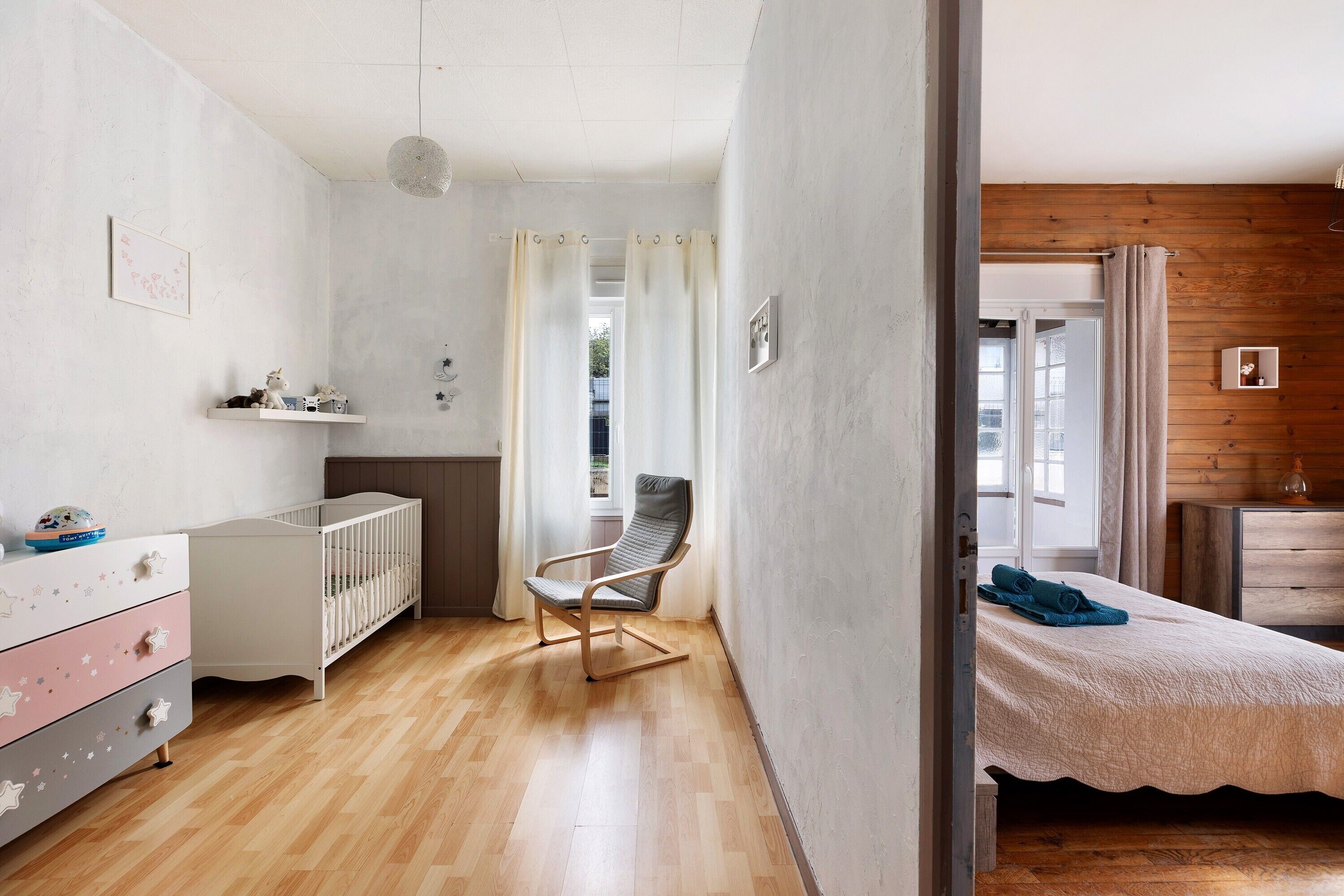 A room with a crib, a rocking chair, a bed, and a wooden wall.