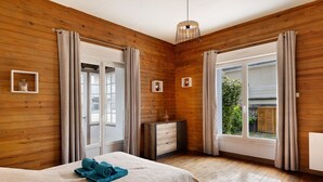 A bedroom with wooden walls, a bed with a beige blanket, a bedside table, and a window with curtains. - Holiday Home 'Gîte Le Rabelais' with Private Pool, Private Terrace and Wi-Fi (Thésée)