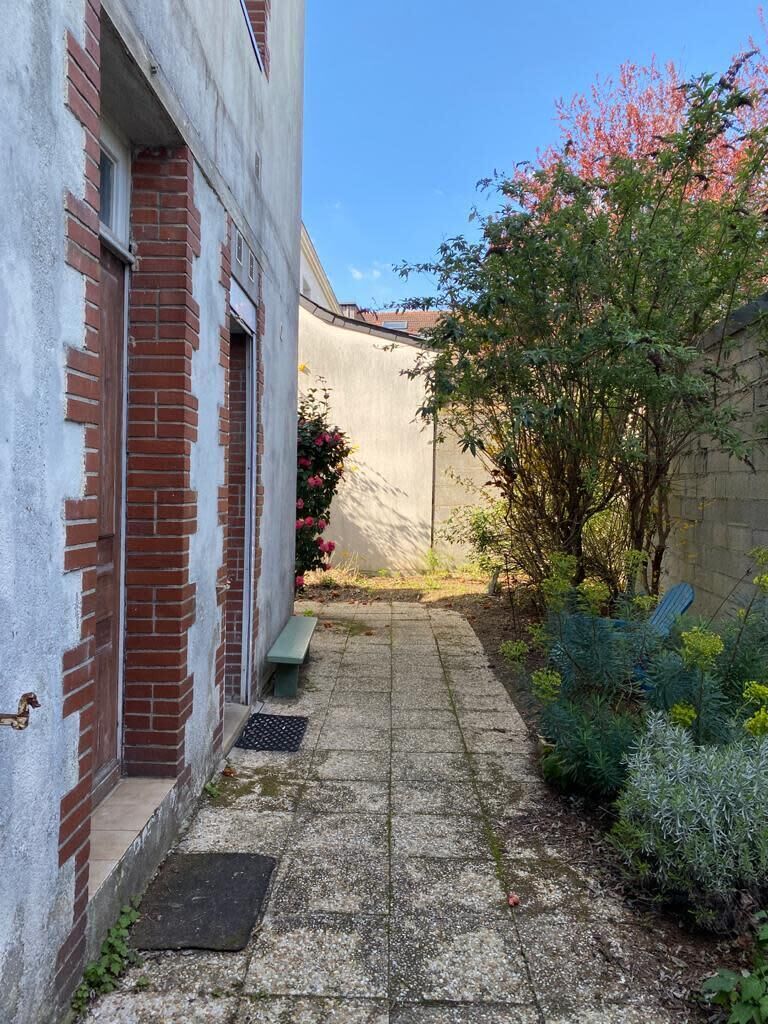 Un estrecho callejón con un banco, una pared de ladrillo y un árbol de flores rosadas.