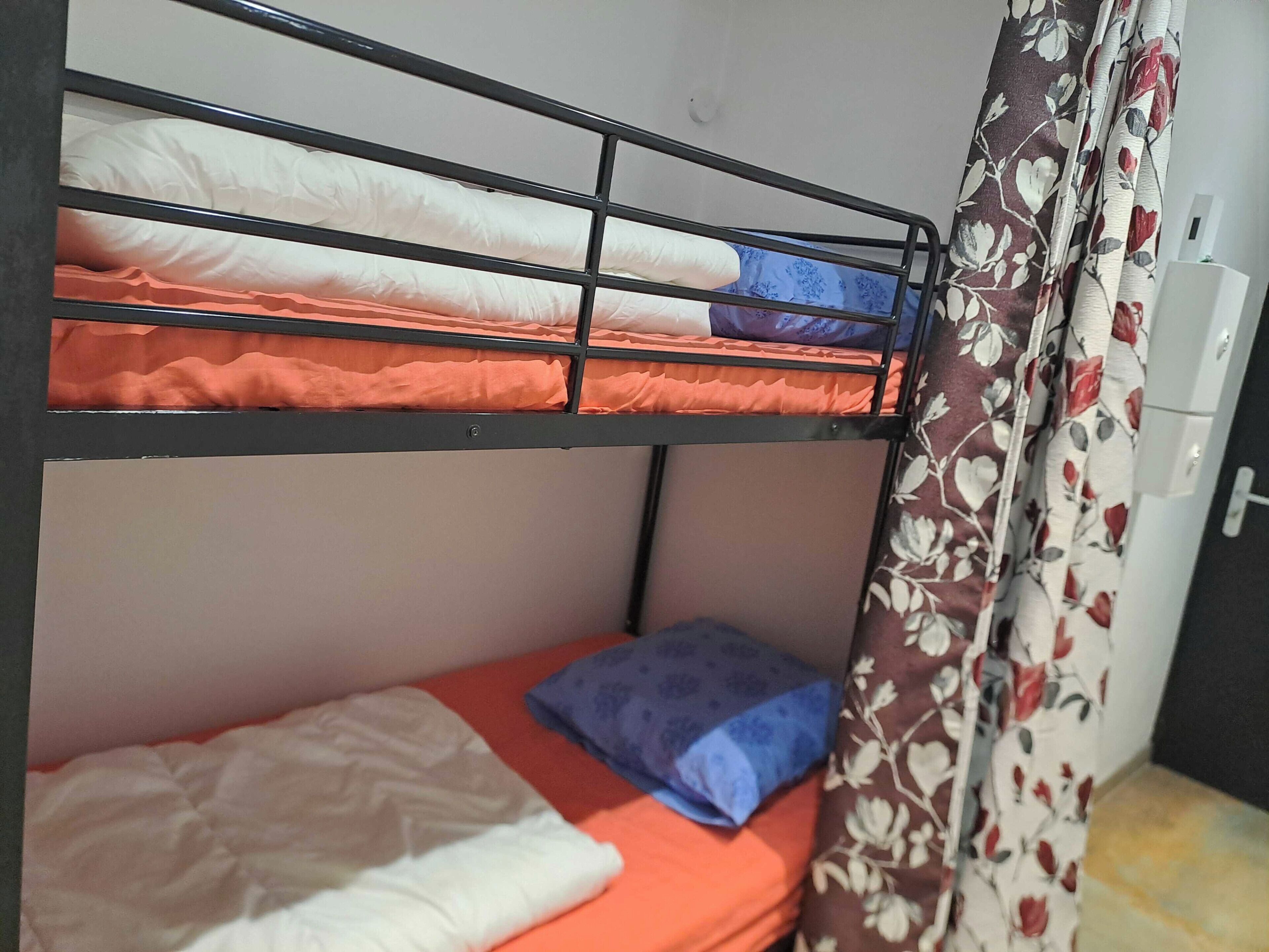 A bunk bed with two levels, a curtain with a floral pattern, and a small white cabinet.
