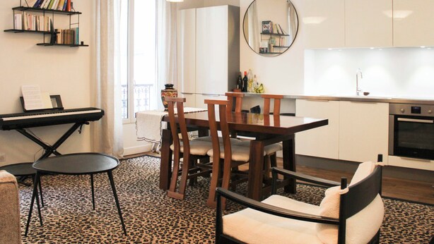 Een moderne keuken met witte kasten, een eettafel met stoelen, een piano en een boekenkast.