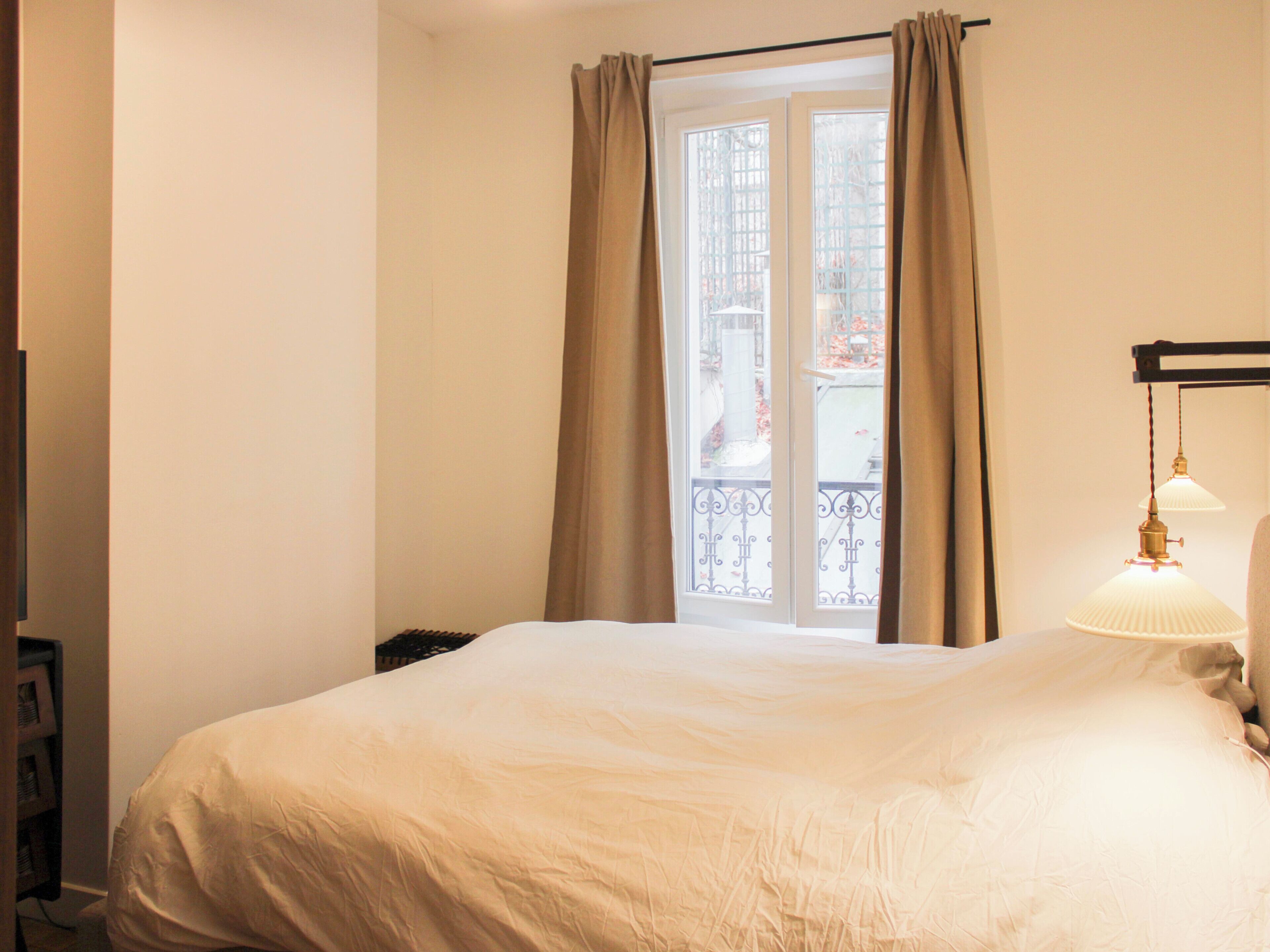 Une chambre d’hôtel avec un lit, une fenêtre avec des rideaux et une lampe.