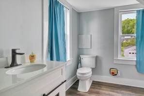 Un baño con lavamanos blanco, inodoro y ventana con cortinas azules.