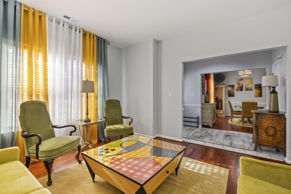A living room with two armchairs, a coffee table, and a dining area with a chandelier.