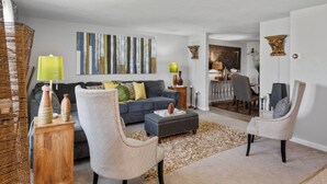 Uma sala de estar moderna com um sofá cinzento, duas poltronas, uma mesa de centro e uma área de refeições com mesa e cadeiras.
