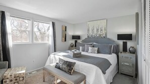 Quarto com cama grande, mesas de cabeceira, um banco e janela com cortinas.