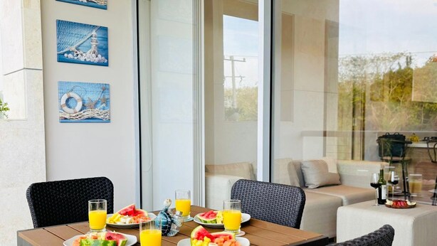 A dining area with a table set for breakfast, featuring plates of fruit and juice, and a view of the outdoors through large windows. - Espacioso y Confortable Bai Kristal (Cartagena de Indias)